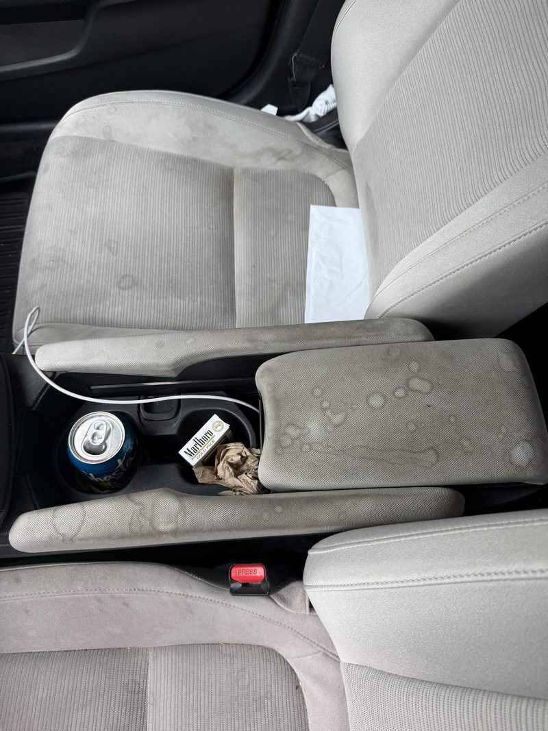 Grey cloth front seats and centre console before cleaning, with stains, crumbs and litter
